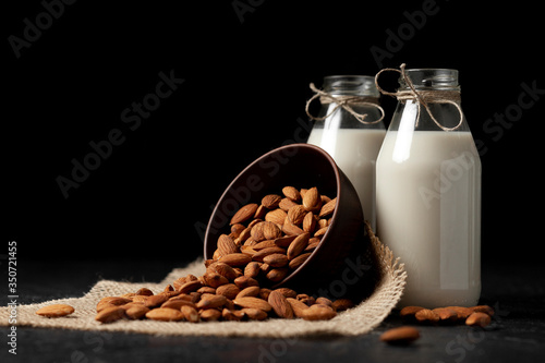 lactose-free almond milk in bottles with nuts on a dark black table  vegetarian milk drink  healthy milk product