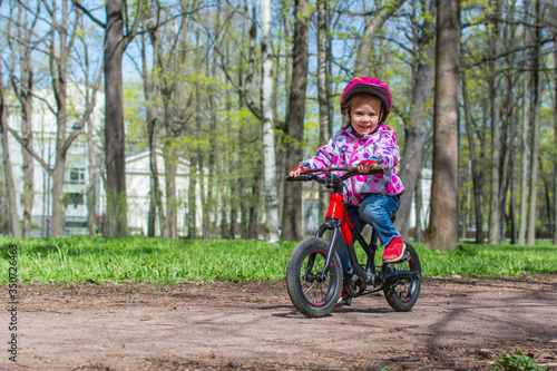 Little cute girl is riding a bicycle in the spring park. Child learning to drive a bicycle on a path outside.