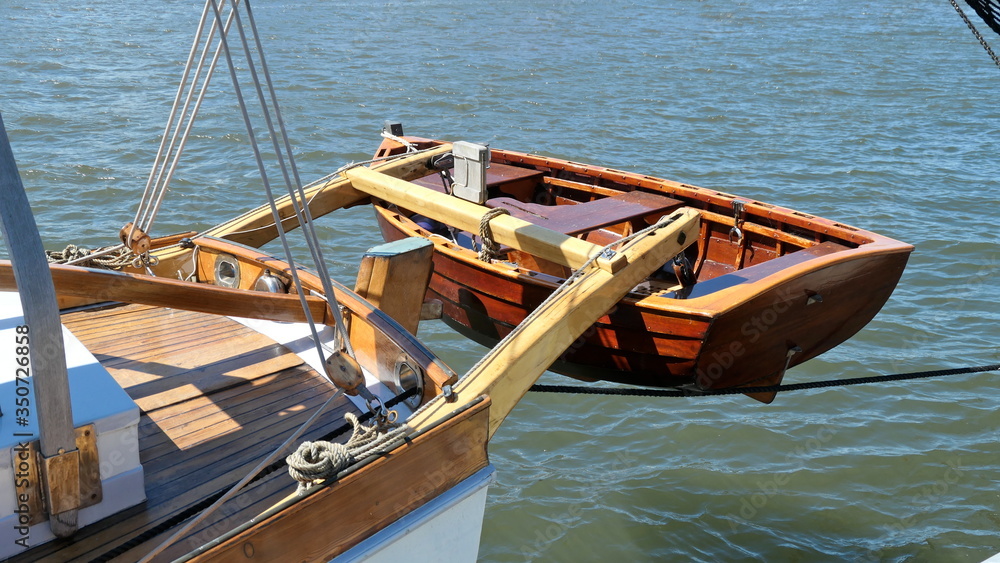 Dinghy, small rowing boat, made of mahogany wood, attached to the stern of a vintage sailing yacht