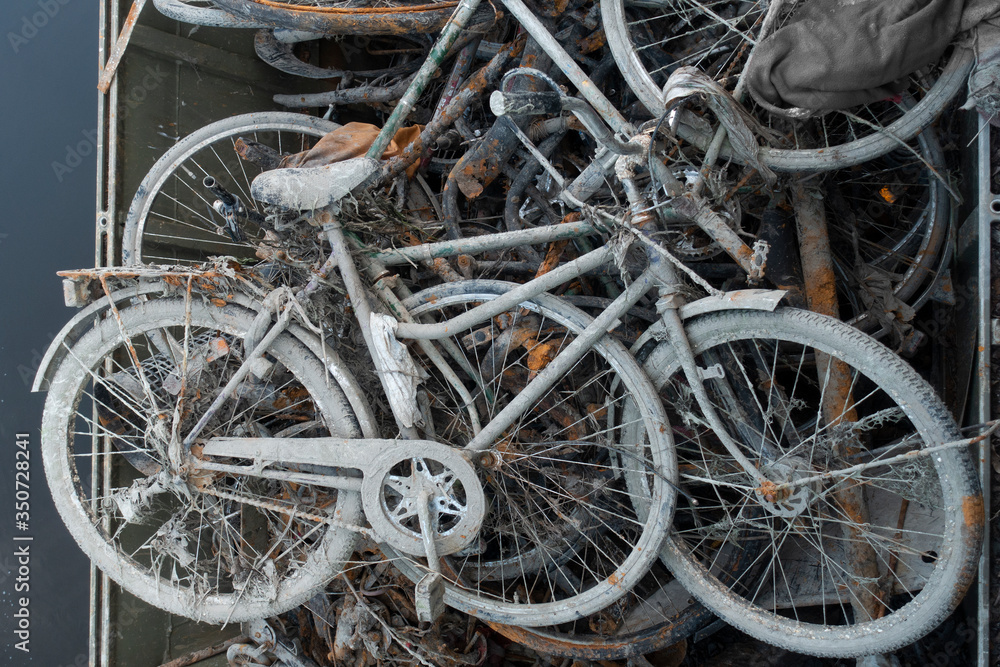 Skip with heap of rusty muddy bicycles retrieved from a river