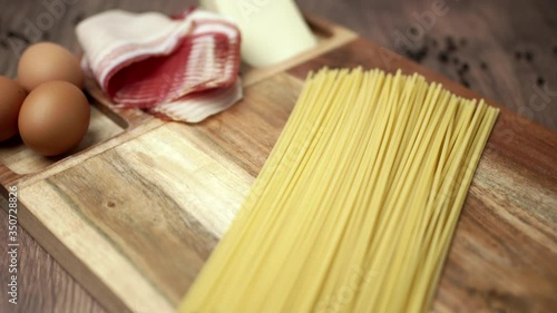 Camera moving and capturing close up of pasta/spaghetti carbonara ingredients on a wooden board on a wooden brown dark table. Carbonara ingredients: eggs, pancetta, pecorino cheese nicely decorated