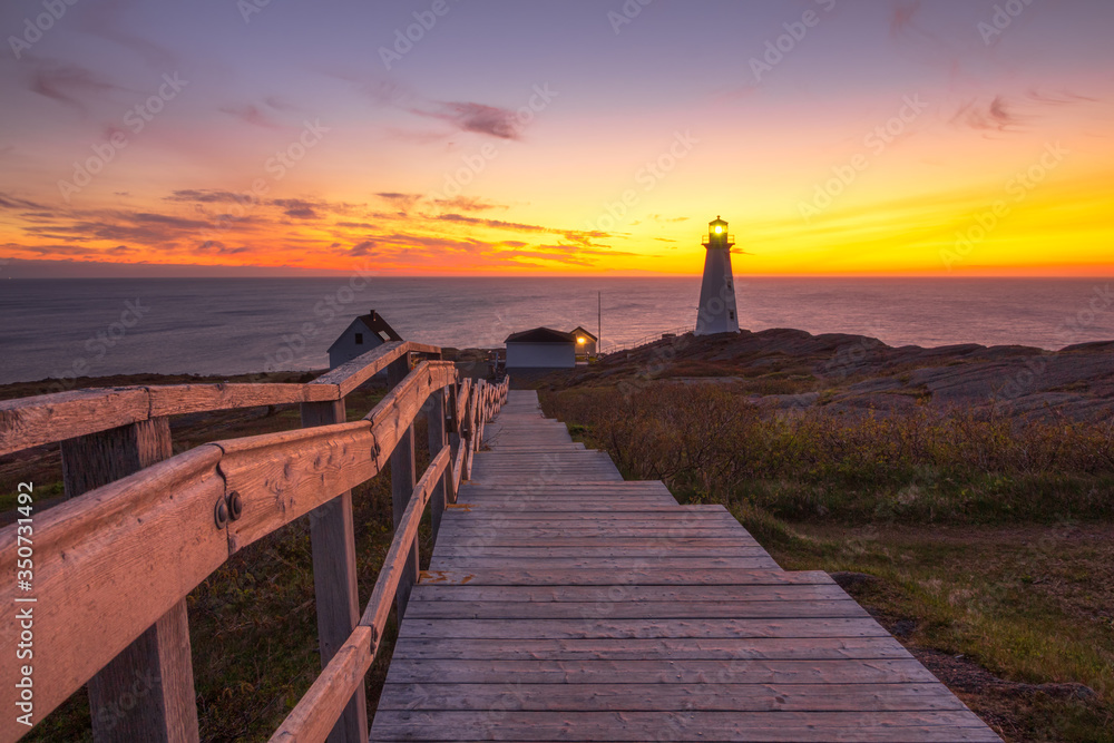 Wooden staircase and boardwalk at a beautiful sunrise, overlooking a white lighthouse sitting at the edge of a rocky cliff.  Cape Spear National Historic Site, St Johns Newfoundland. 