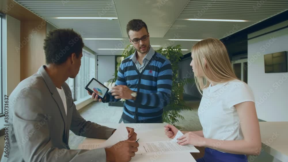 Side view of black man with coworkers at table reading papers and using tablet in team at table. Side view of black man with coworkers at table reading papers and using tablet in team at table.
