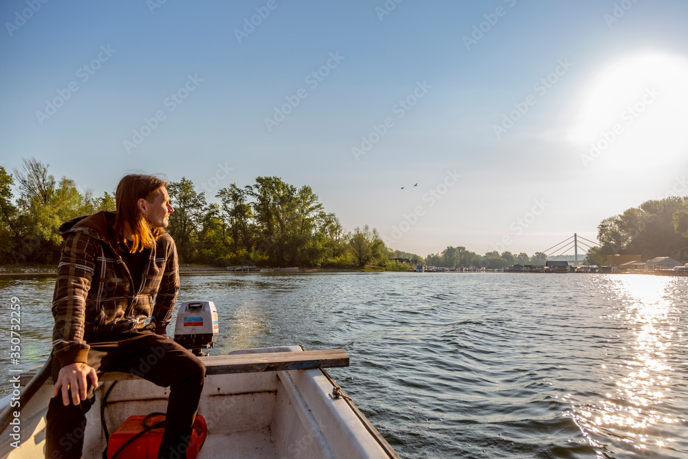 Sad man is riding a boat over river in sunset