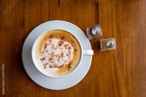 Cappuccino with froth texture and ground cinnamon in a white coffee cup and saucer on a wooden table. Top view. Coffee energy drink in the morning.