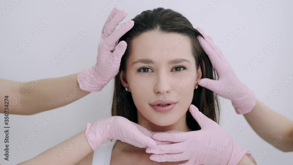 Brunette girl has facial massage. Client is in beauty studio. Masseur wears pink gloves. Brunette girl has facial massage. Client is in beauty studio. Masseur wears pink gloves.