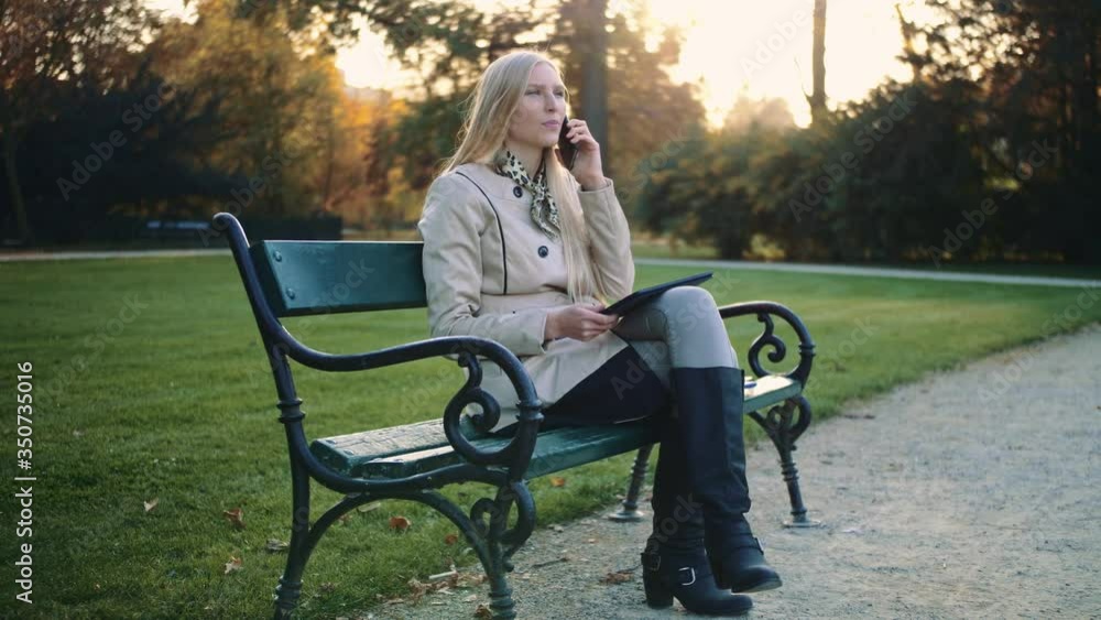 Young blonde girl with tablet computer and cellphone sitting on park bench. 4K Young blonde girl with tablet computer and cellphone sitting on park bench. 4K