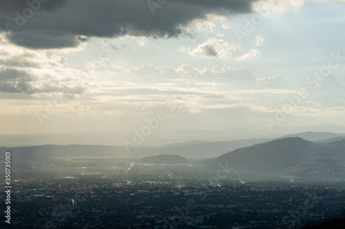 an eerie, misty, fog hovers over a city at the foot of mountains on a cloudy spring afternoon