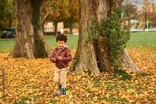 Outdoor autumn portrait of cute african boy  wearing brown leather jacket  child having fun in park