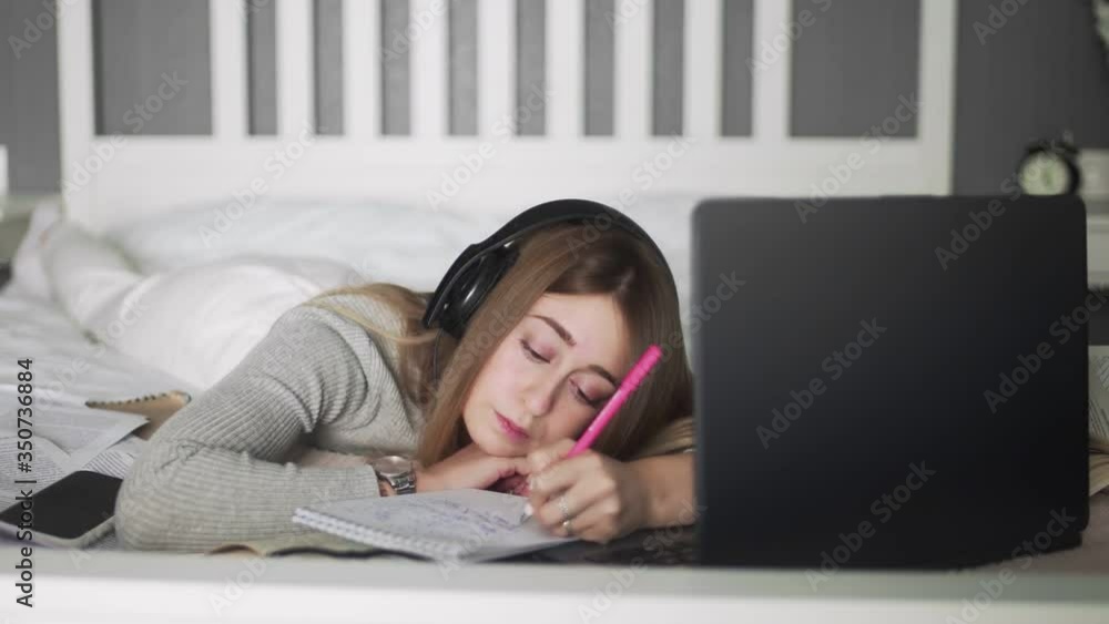 Young woman with headphones lying on the bed and making hotes on notebook Young woman with headphones lying on the bed and making hotes on notebook