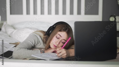 Young woman with headphones lying on the bed and making hotes on notebook photo