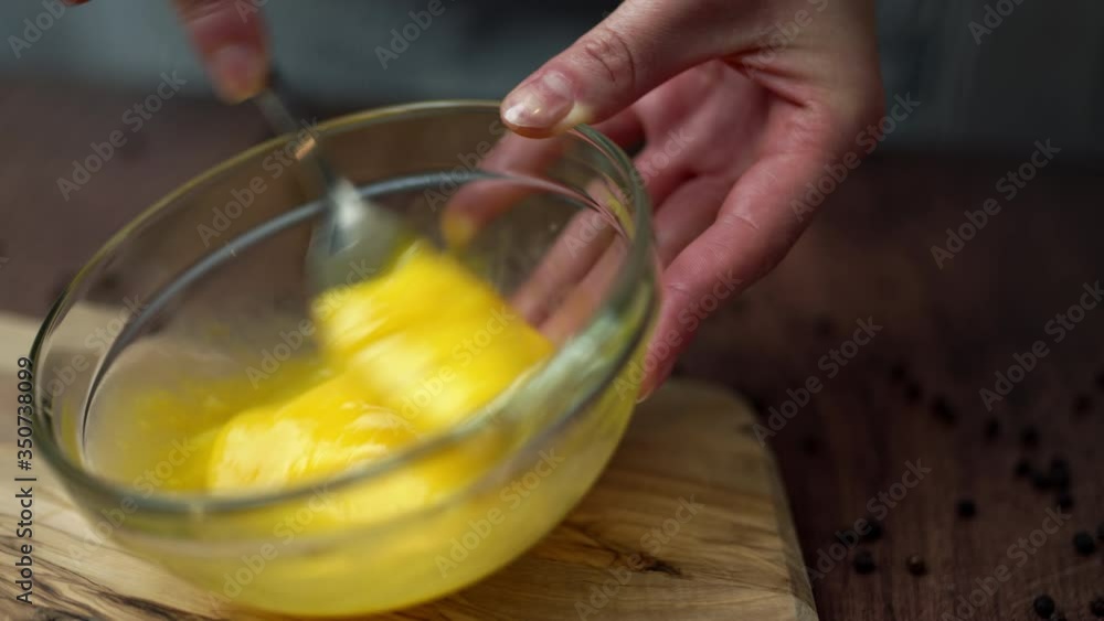 Close-up of a woman's hand whisking/mixing eggs in a transparent glass bowl. Slow-motion beating egg process. Close-up of a woman's hand whisking/mixing eggs in a transparent glass bowl. Slow-motion beating egg process.