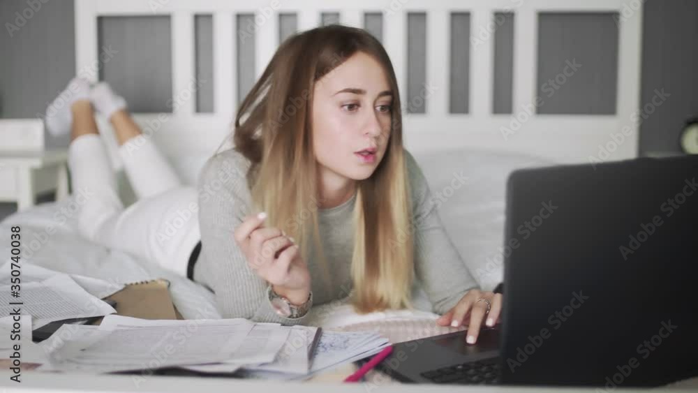 Young woman work at home. Woman lays on the bed and listens to the musics Young woman work at home. Woman lays on the bed and listens to the musics