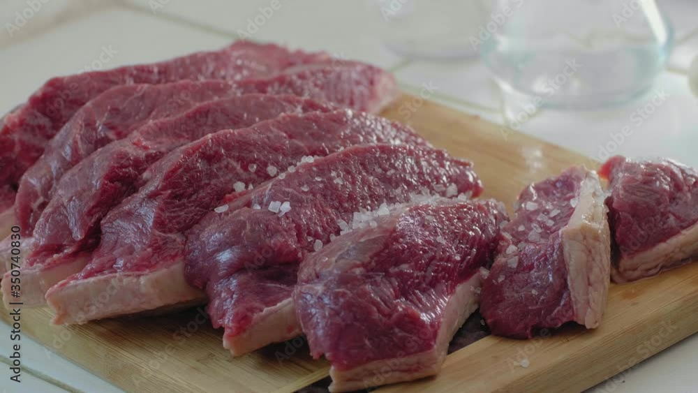 A raw chopped up top sirloin steak being seasoned with sea salt.