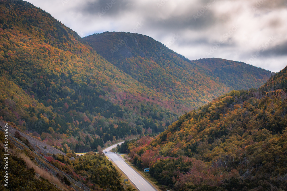 Fototapeta premium Autumn colors of the Cape Breton as the sun rays fall on the valley. Fall foliage of the mountains with multi colored deciduous trees, Cabot Trail, Cape Breton Nova Scotia 