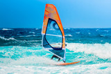 summer sports: windsurfer riding the waves during a sunny summer afternoon on the blue ocean water.