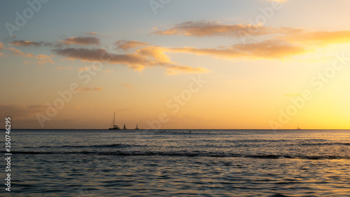 Warm sunset on the ocean with sailing boats located on the horizon, shot at Waikiki beach, Honolulu, Hawaii, USA 
