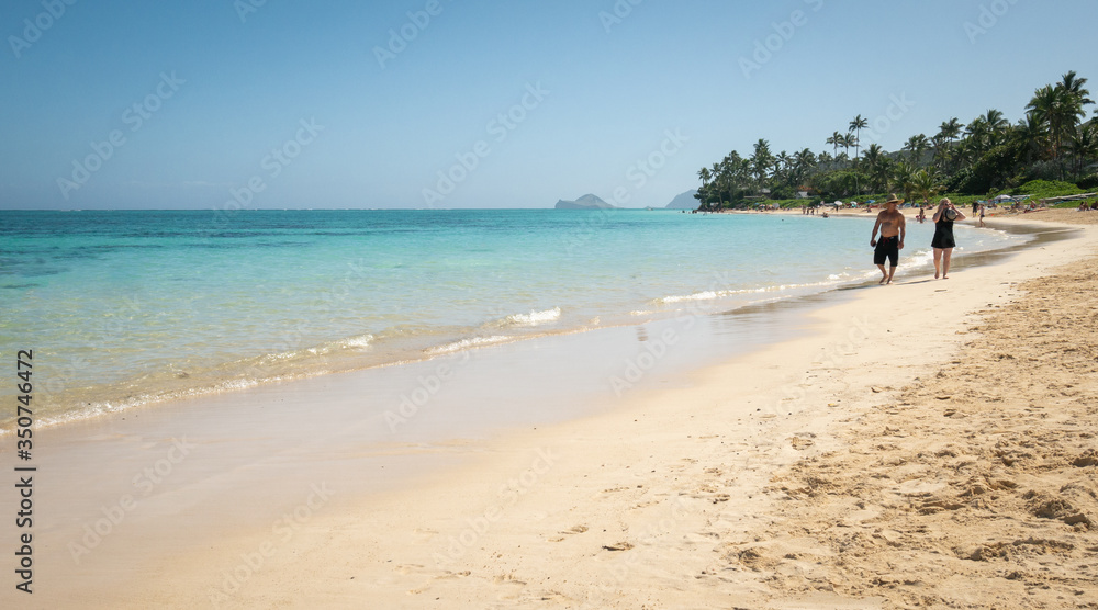 Couple walking on tropical sandy beach with azure waters, shot at Kailua Beach, Oahu, Hawaii, USA
