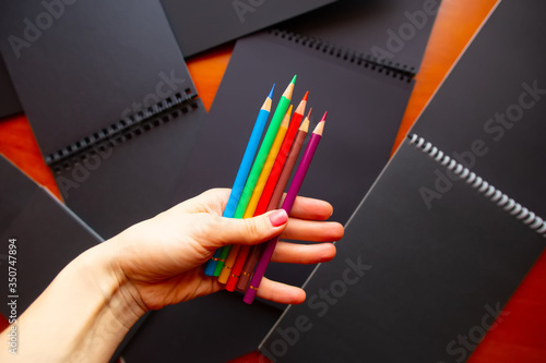 A hand holding bright colored pencils in front of black paper sketch boooks photo