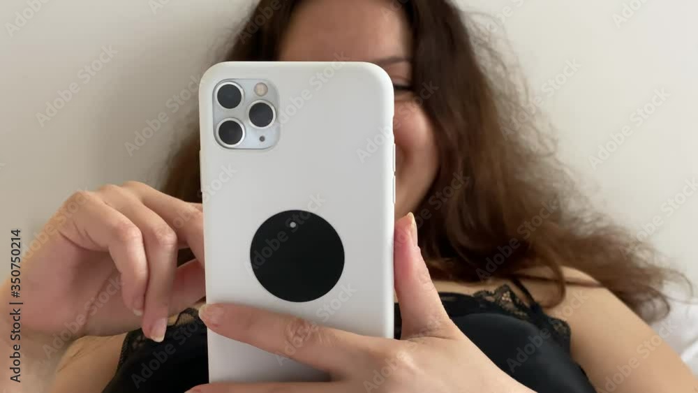 Woman holding mobile phone while lying in bed at home. Woman holding mobile phone while lying in bed at home.