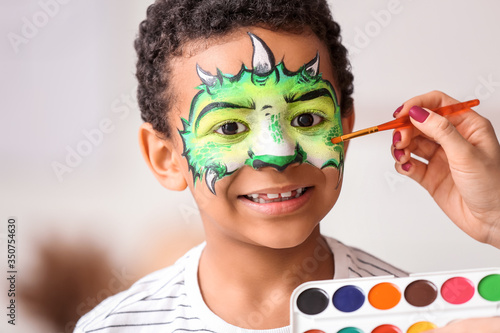 Woman painting face of African-American boy at home