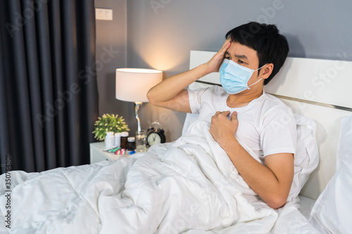 sick man in medical mask is headache and suffering from virus disease and fever in a bed, coronavirus (covid-19) pandemic concept.