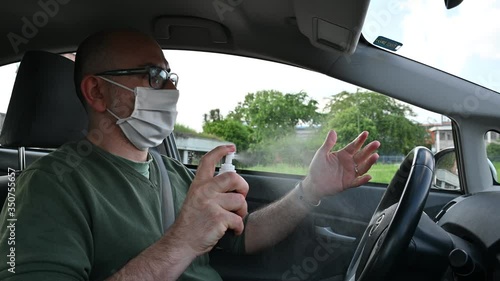 Turin, Piedmont, Italy. May 2020. Coronavirus pandemic: portrait of a Caucasian man driving with a white mask. He sprays disinfectant on his hands, rubs them and puts the bottle away.