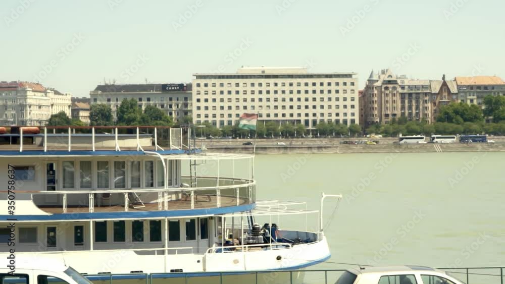 A river cruise boat docked in the port along the Danube River with a Hungarian flag flying from its bow. A river cruise boat docked in the port along the Danube River with a Hungarian flag flying from its bow.
