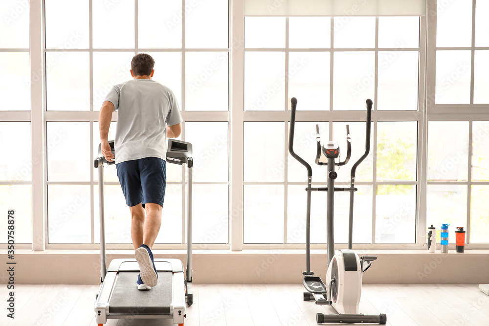 Fototapeta premium Young man training on treadmill in gym