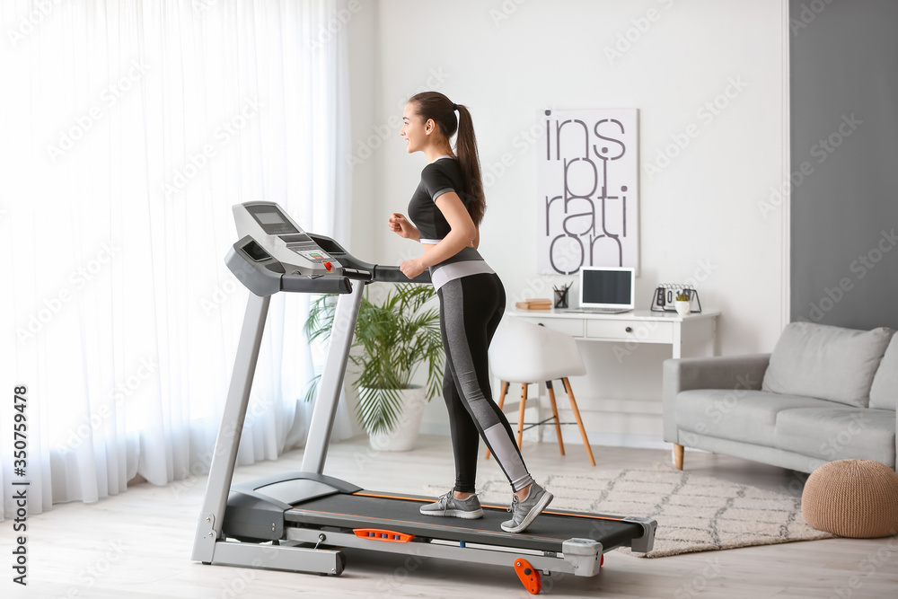 Fototapeta premium Sporty young woman training on treadmill at home
