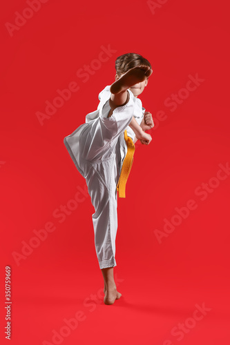Cute little boy practicing karate on color background