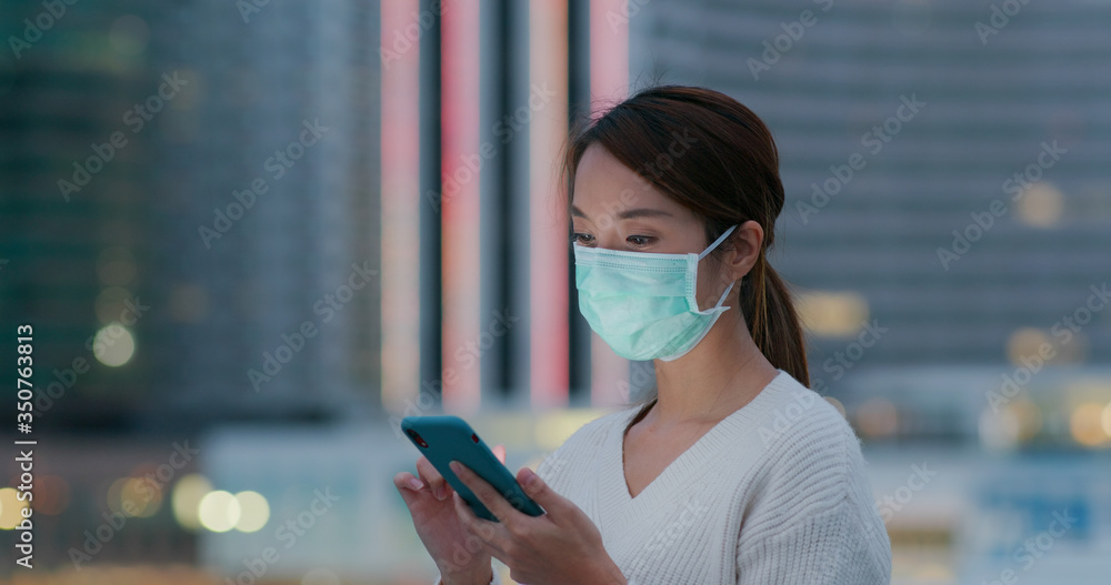 Woman wear medical face mask and use of cellphone in city at sunset