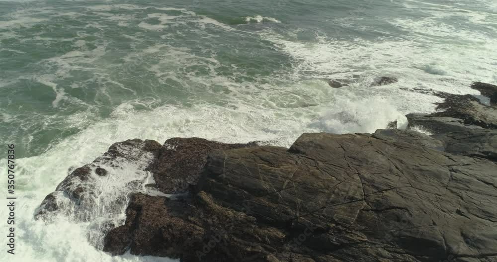 Aerial shot of waves crashing on rock formation in sea, drone panning over beach on sunny day - Luderitz, Namibia