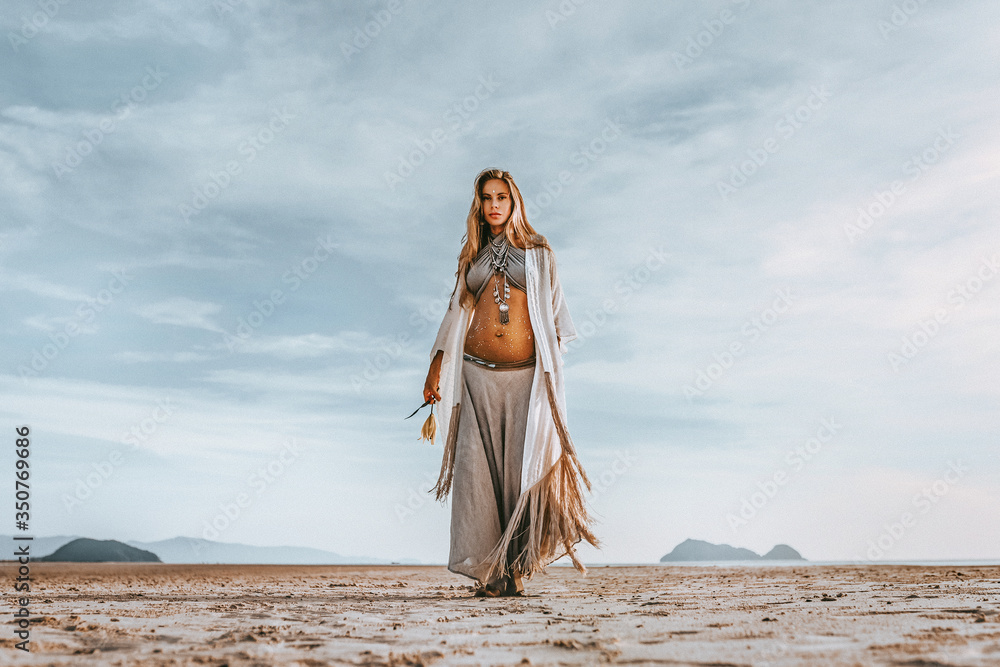 Fototapeta premium beautiful young stylish pregnant woman with boho accessories walking on the beach at sunset