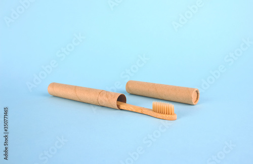 Natural bamboo toothbrushe packed in reusable paper tube on blue background with copy space. Sustainable lifestyle and plastic free concept, bathroom essentials in zero waste home, mockup