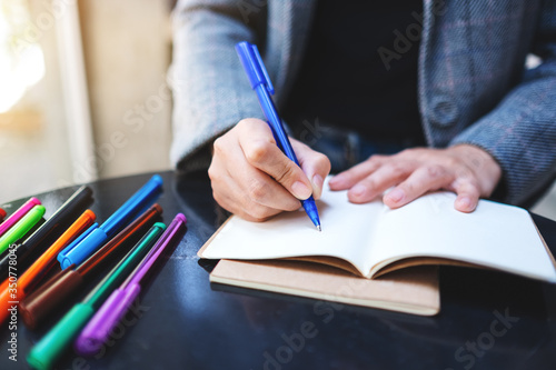 Closeup image of a woman writing on a blank notebook with colored pens on the table