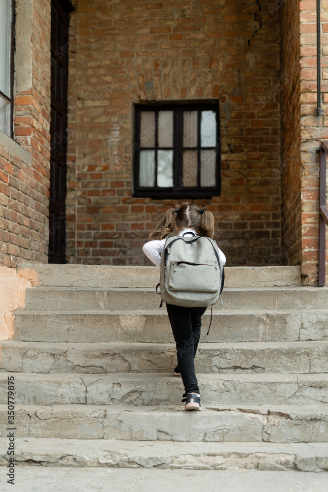 Girl schoolgirl climbs the stairs. She goes to school to get knowledge. On the back of the child is a backpack. School uniforms and education.