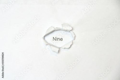 Word nine on white isolated background, the inscription through the wound hole in the paper. Stock photo for web and print with empty space for text and design.