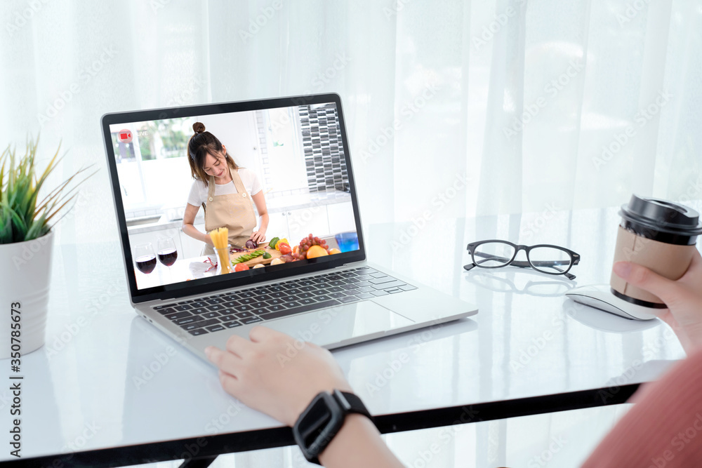 Fototapeta premium Rear view shot, Asian woman watching live video steaming online chef teach cooking food prepare with vegetable healthy diet menu and many fruit for dinner, staying from home self-isolation concept.