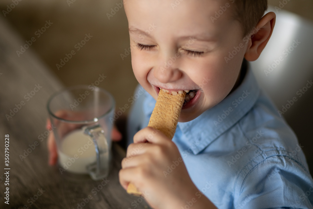 Baby boy eating cookies close-up. The boy bit his biscuits with his teeth. In the hand, the child holds a glass with milk. The pleasure of eating. Baby boy eating cookies close-up. The boy bit his biscuits with his teeth. In the hand, the child holds a glass with milk. The pleasure of eating.