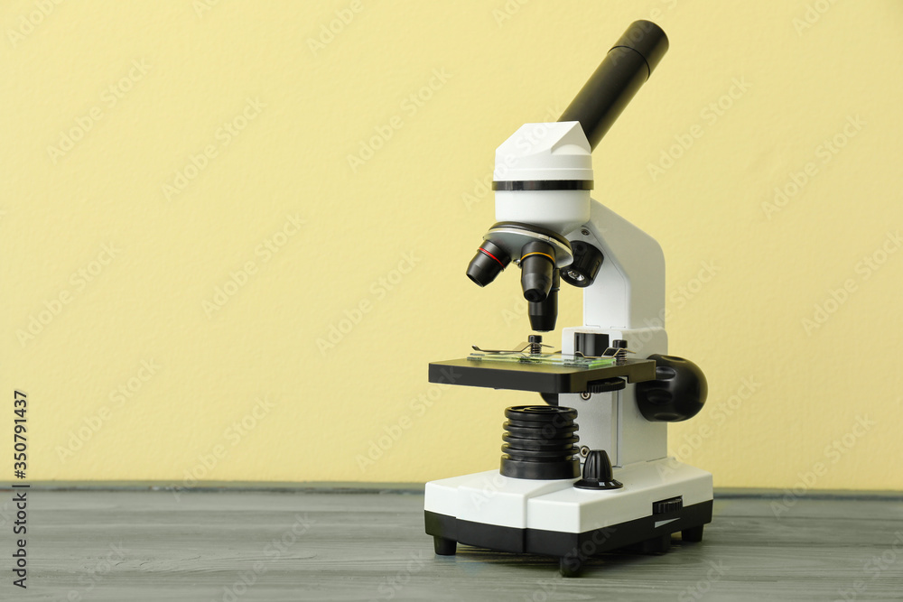 Modern microscope on table against color background