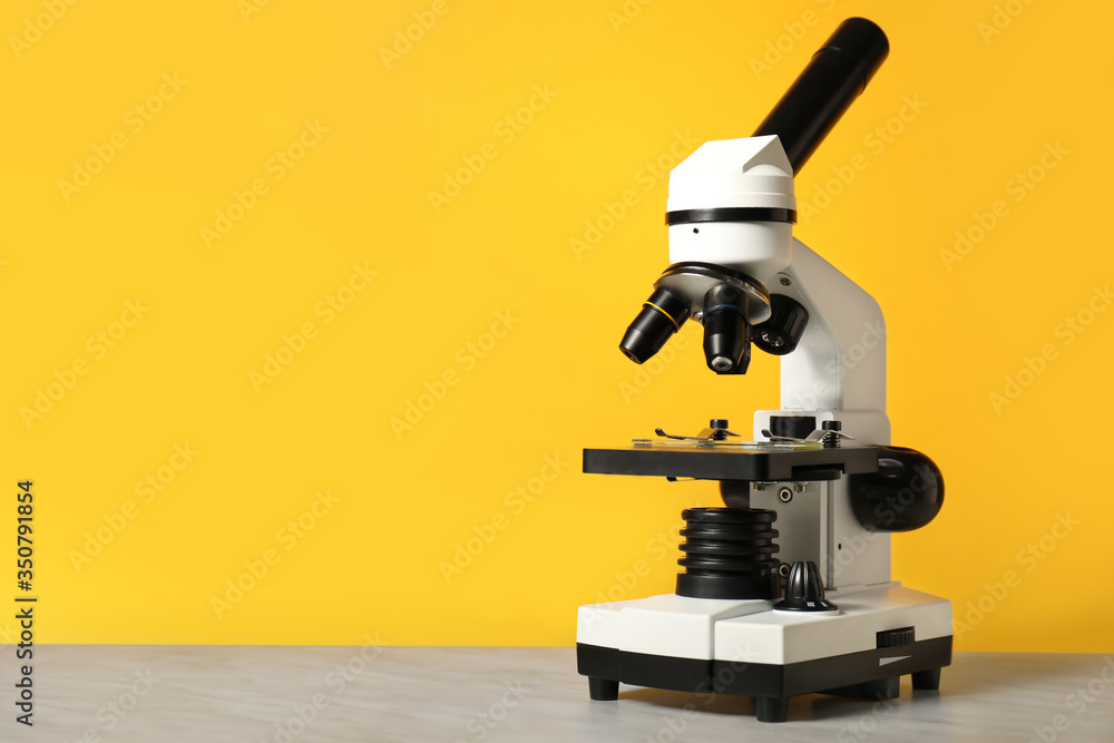 Modern microscope on table against color background Modern microscope on table against color background