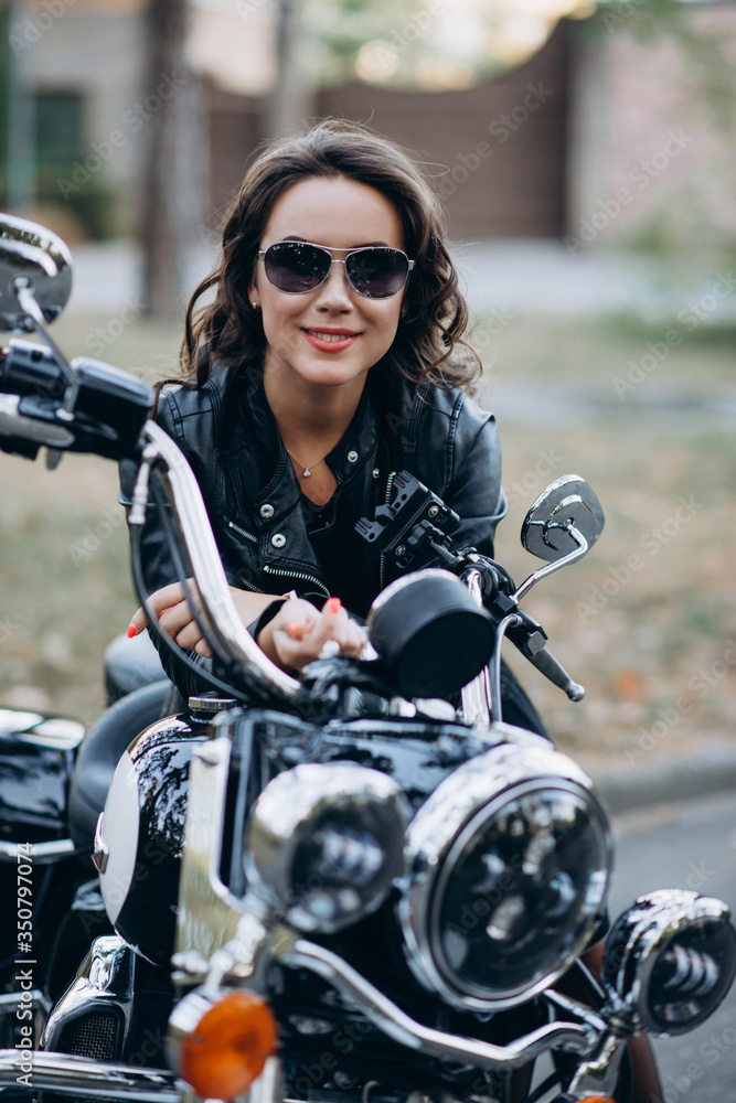 Young beautiful biker woman in glasses and a leather jacket on a motorcycle. The concept of speed and freedom. Soft sective focus Young beautiful biker woman in glasses and a leather jacket on a motorcycle. The concept of speed and freedom. Soft sective focus