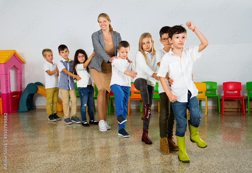 Obraz premium Positive female teacher playing circle game with children in classrom