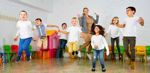 Tableau sur toile Positive female teacher and group of schoolkids jumping in classroom