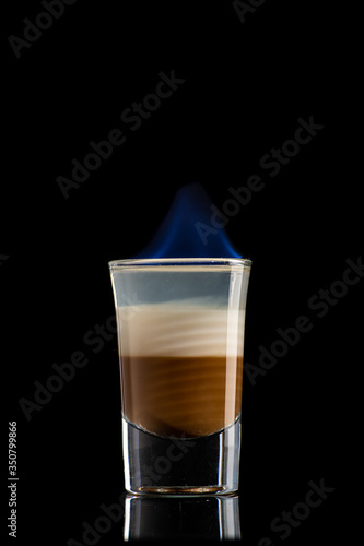 coffee cream alcoholic cocktail B52 in three layers was set on fire and burns with a blue flame in a shot glass on a black background