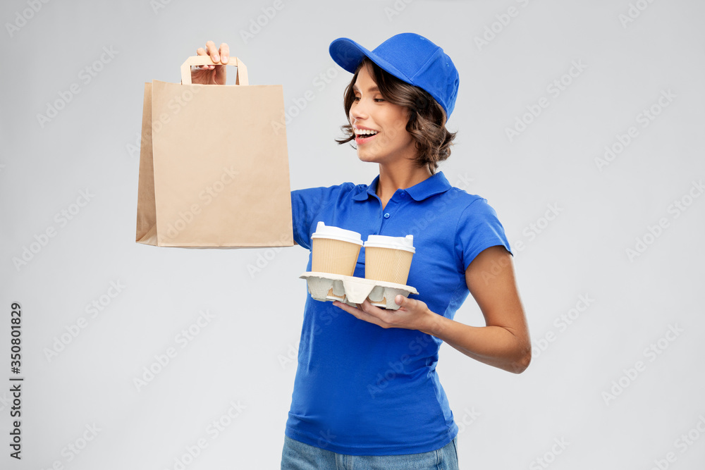 service and job concept - smiling delivery girl in blue uniform with takeaway food in paper bag and hot drinks in disposable cups over grey background service and job concept - smiling delivery girl in blue uniform with takeaway food in paper bag and hot drinks in disposable cups over grey background