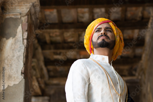 Low angle portrait of a young Indian man with ethnic wear with turban in an old vintage house. Indian lifestyle