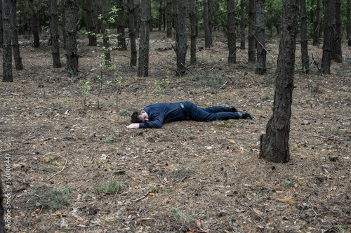 Murder in the woods. The body of a man in a blue shirt and trousers lies on the ground among the trees in the forest. Victim of an attack.