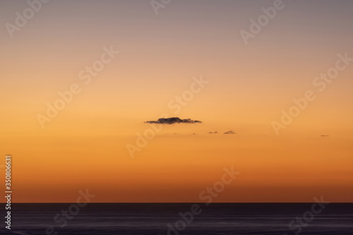 View of small dark cloud over black ocean waters at sunset © Emagnetic